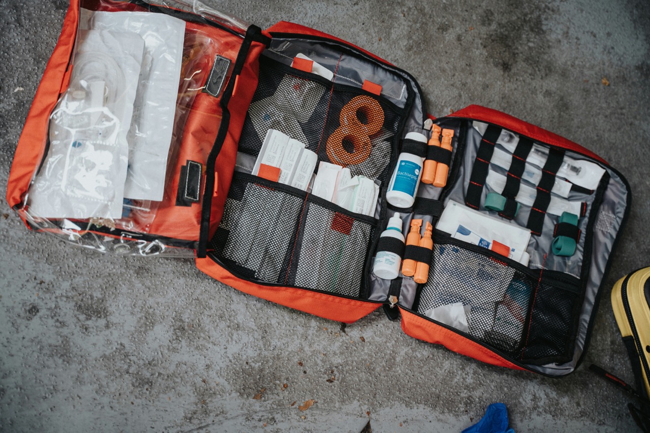 Open workplace first aid kit showing organized medical supplies including bandages, gauze, antiseptic bottles, medical tape, scissors, and emergency equipment on orange background